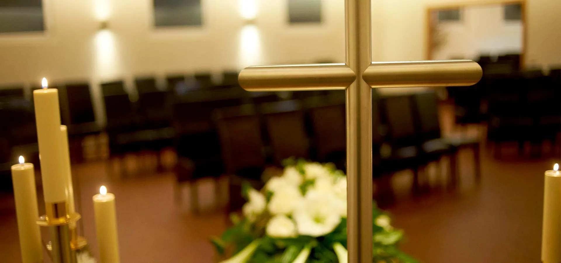 Goldenes Kreuz vor weißen Blumen in der Trauerhalle der Abschiedsräume „Seelenfrieden“