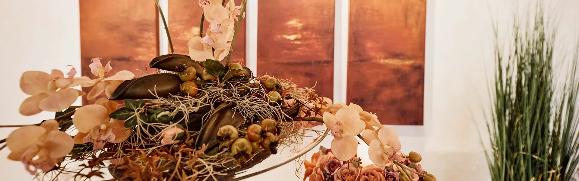 Herbstliches Blumengesteck mit Orchideen vor warm beleuchteten Wandbildern in den Abschiedsräumen